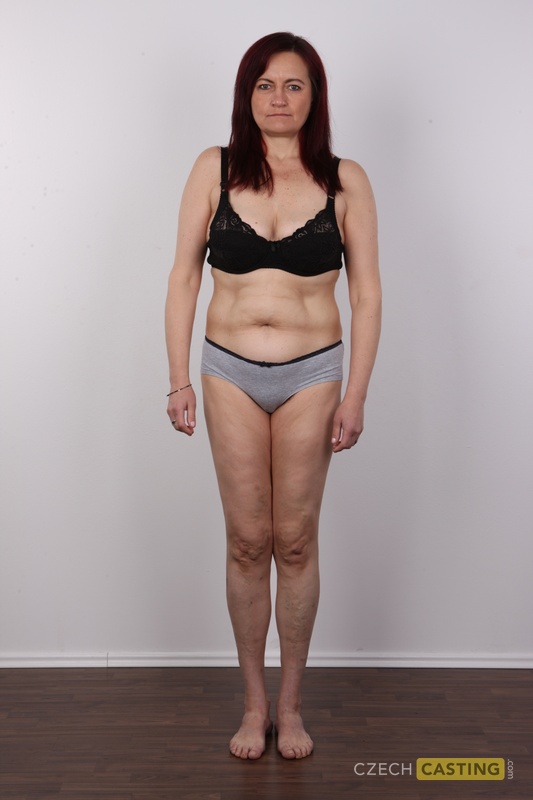 Mature woman with red hair stands straight while getting completely naked