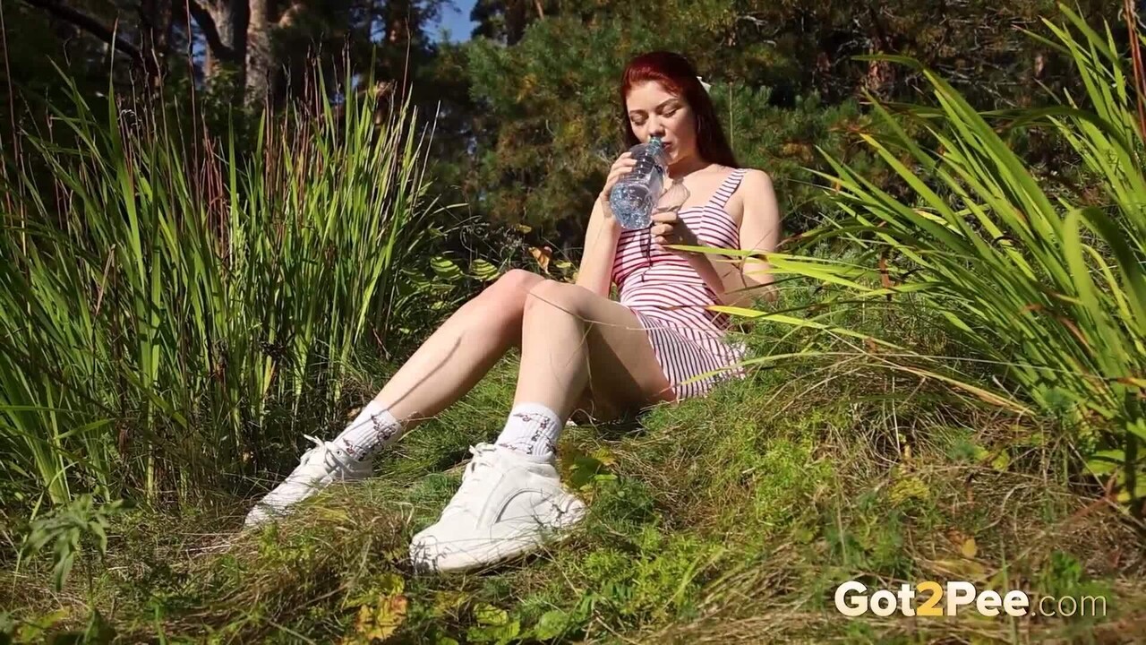 Redheaded girl Foxy Dream leans back in the grass to take an outdoor piss