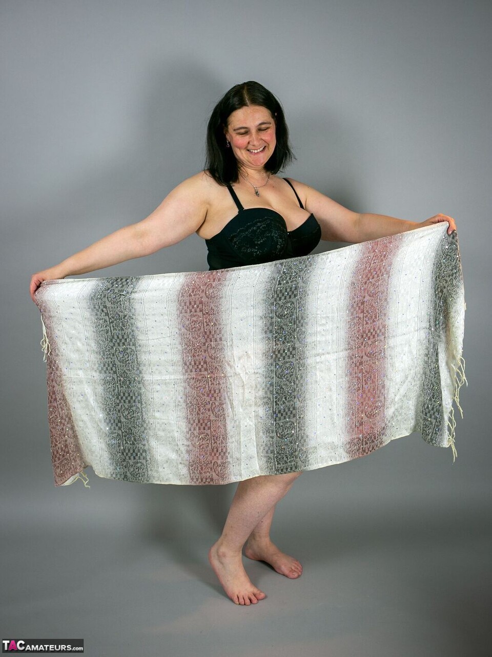Brunette amateur pulls on sheer fabric while posing naked for her photographer