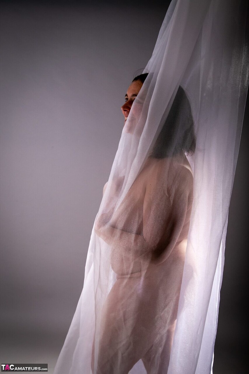 Brunette amateur pulls on sheer fabric while posing naked for her photographer
