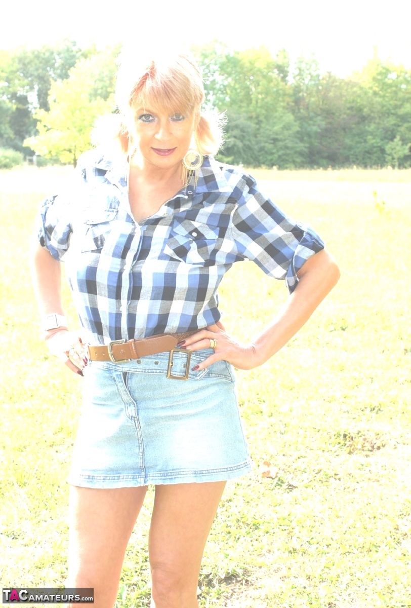 Mature blonde removes a short skirt while spreading on a wooden fence