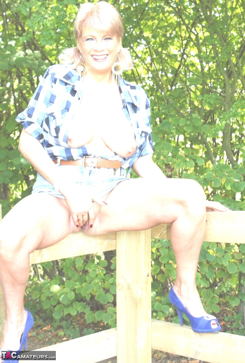 Mature blonde removes a short skirt while spreading on a wooden fence