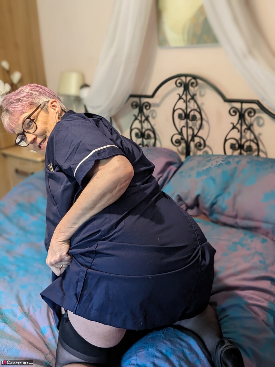 Older nurse Layla Bird removes her uniform before masturbating on a bed