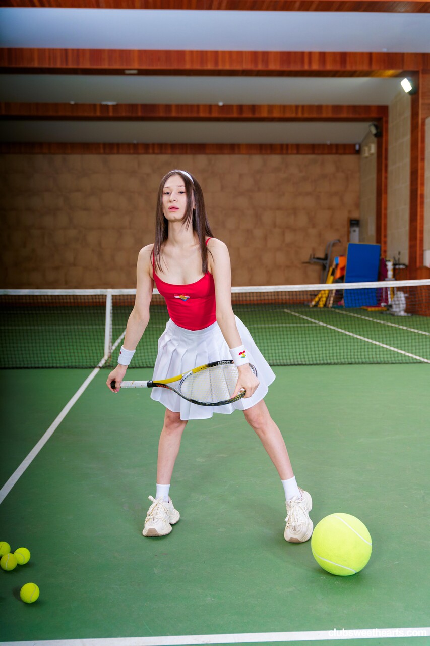 Young beauty with long brown hair removes tennis attire to pose nude on a court