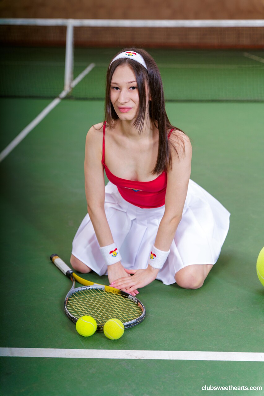 Young beauty with long brown hair removes tennis attire to pose nude on a court